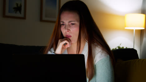 Anxious-Woman-Sitting-On-Sofa-At-Home-At-Night-Looking-At-Laptop-Concerned-About-Social-Media-Or-Bad-News